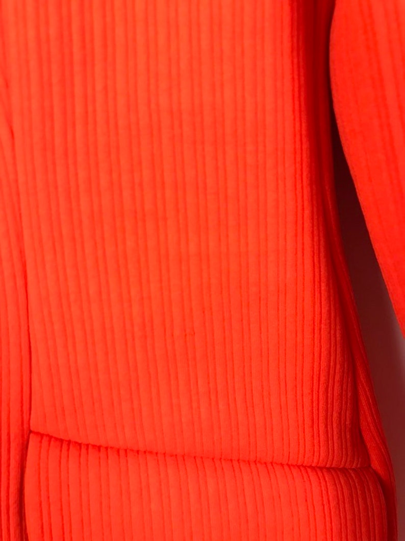 May include: Close-up of a bright orange ribbed fabric. The fabric has a smooth texture and a subtle sheen.