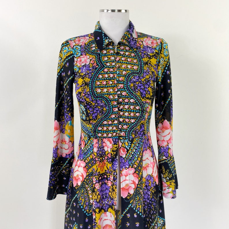 Puede incluir: Un vestido largo de manga larga, negro, con estampado floral en tonos rosa, morado, amarillo y azul. El vestido tiene un frente abotonado y un cuello.