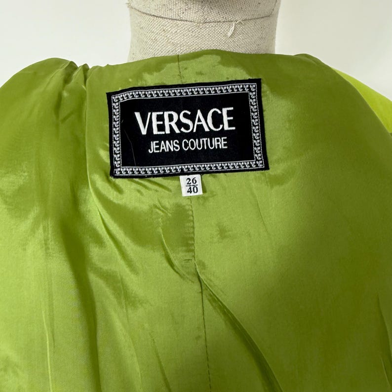 May include: Close-up of a lime green garment's interior. A black and white label reads "VERSACE JEANS COUTURE". Below the label are the numbers "26" and "40".