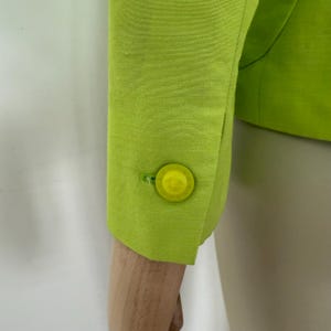 May include: Close-up of a lime green blazer sleeve with a matching button. The button is round and has a yellow center. The fabric has a subtle texture.
