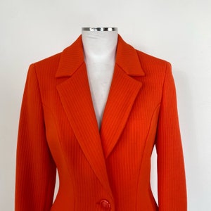 May include: A bright orange blazer with a single button closure and a ribbed texture. The blazer has a classic, tailored fit.