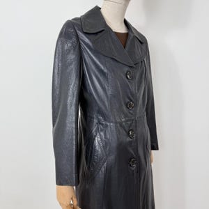 May include: A vintage black leather coat with a classic design. The coat features a notched collar, button-down closure, and a tailored fit. The coat has a textured appearance and a knee-length hemline, offering a timeless aesthetic.