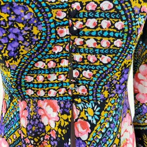 Puede incluir: Una blusa negra, morada, amarilla y azul con estampado, con botones en la parte delantera y mangas largas.
