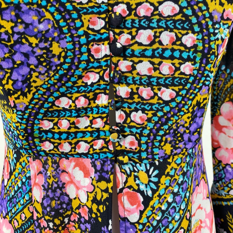 Puede incluir: Una blusa negra, morada, amarilla y azul con estampado, con botones en la parte delantera y mangas largas.