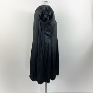 May include: A black satin dress with a flared skirt and a fitted bodice. The dress has short, puffed sleeves and a subtle sheen. The garment is displayed on a mannequin against a plain white background, showcasing its elegant design.