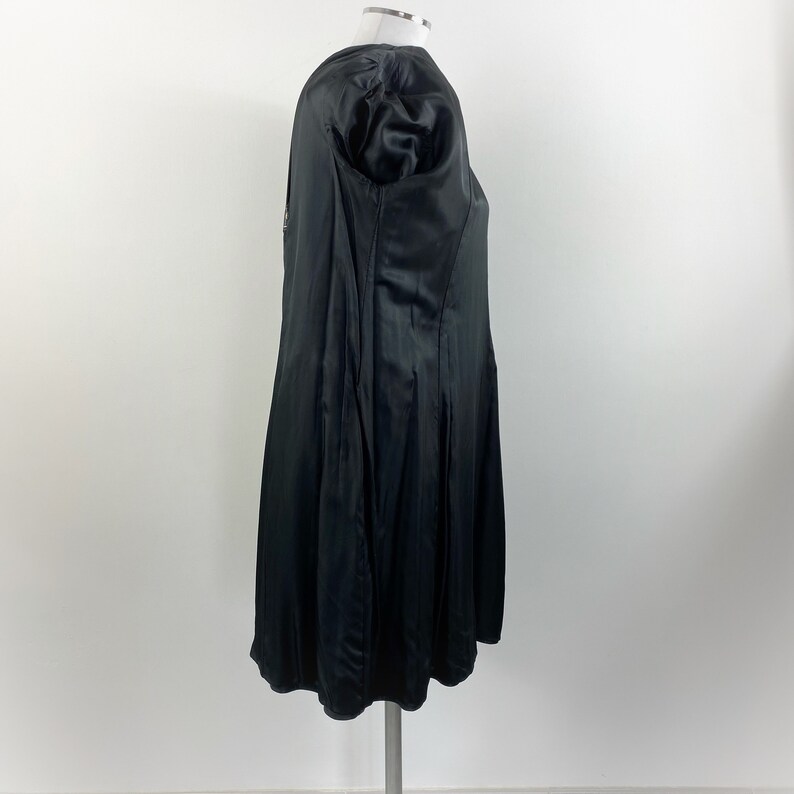 May include: A black satin dress with a flared skirt and a fitted bodice. The dress has short, puffed sleeves and a subtle sheen. The garment is displayed on a mannequin against a plain white background, showcasing its elegant design.