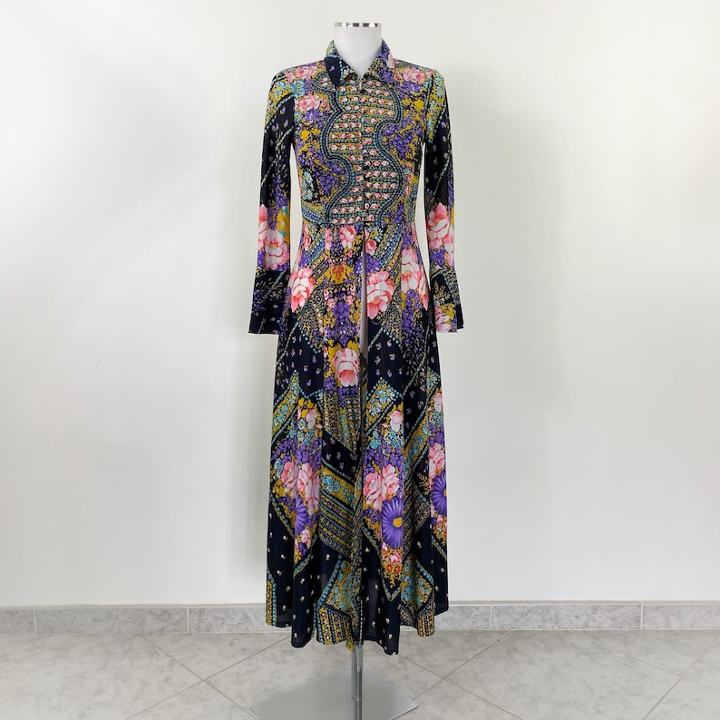 Puede incluir: Un vestido largo de manga larga con fondo negro y estampado floral colorido. El vestido tiene cuello y cierre de botones en la parte delantera.