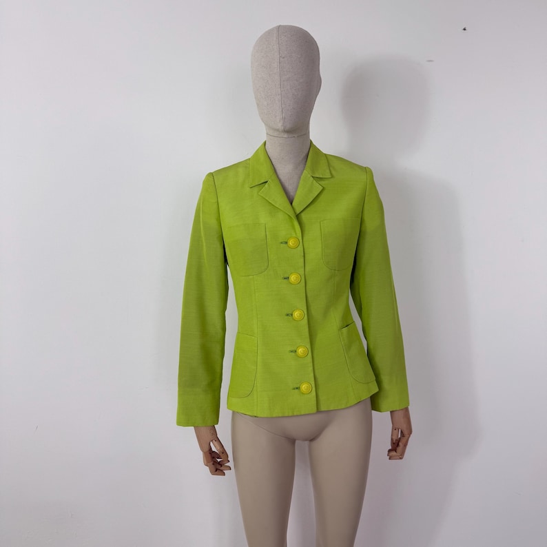 May include: A lime green blazer with a classic tailored design. The blazer features a notched collar, two front pockets, and yellow buttons. The long-sleeved jacket is displayed on a mannequin against a white background.