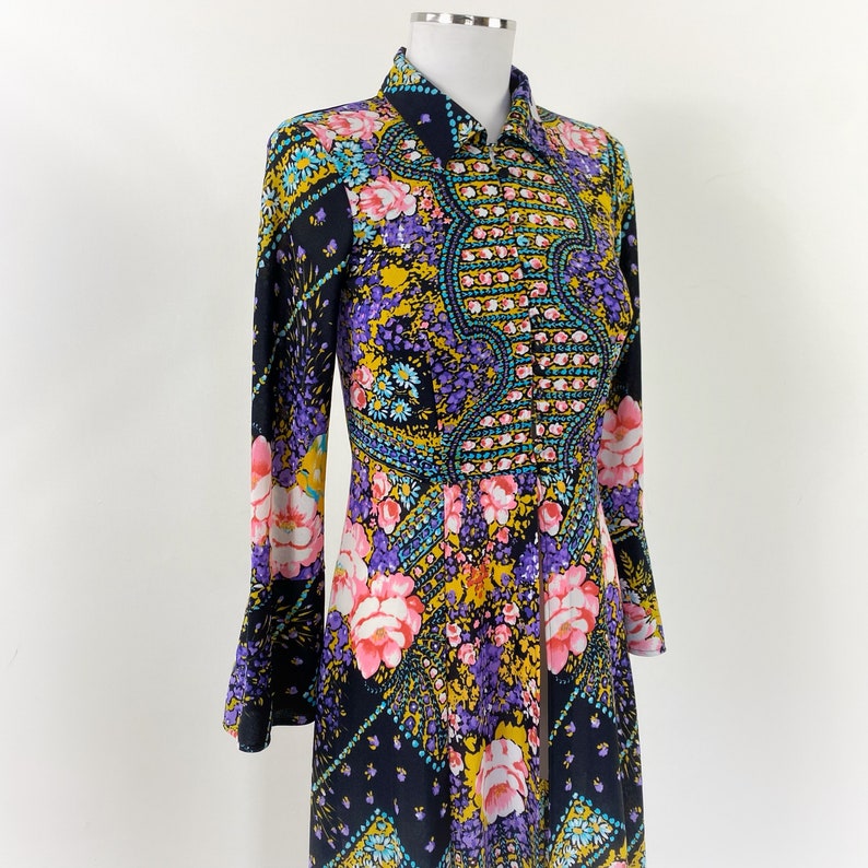 Puede incluir: Un vestido de manga larga con estampado floral y geom&eacute;trico de colores. El vestido tiene un cierre de botones en la parte delantera y un cuello.