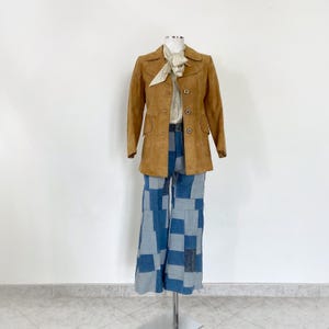 Puede incluir: Una chaqueta de ante marrón con una blusa blanca y pantalones acampanados de mezclilla con parches azules.