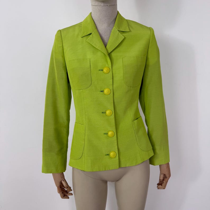 May include: A lime green blazer with a notched collar, long sleeves, and four yellow buttons. The blazer has two front pockets and a tailored fit. The fabric has a subtle texture.