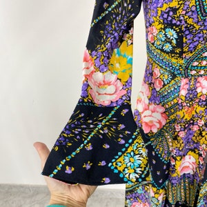 Puede incluir: Un vestido de manga larga con fondo negro y estampado floral colorido. El vestido tiene una manga acampanada con un estampado floral contrastante.