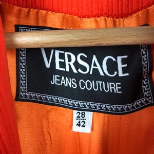 May include: A black label with white text that reads "VERSACE JEANS COUTURE" with a size tag that reads "28/42".