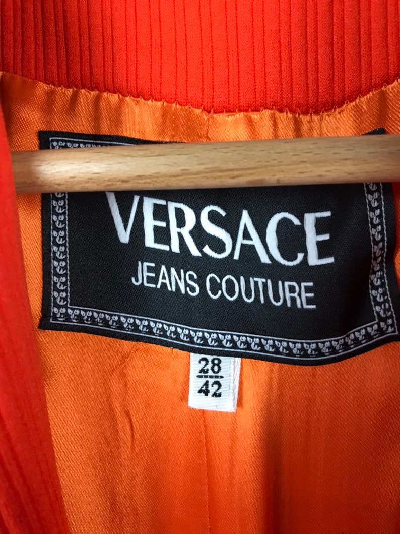 May include: A black label with white text that reads "VERSACE JEANS COUTURE" with a size tag that reads "28/42".