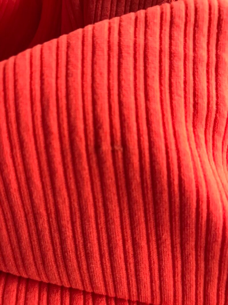 May include: Close-up of a bright orange ribbed fabric. The fabric has a soft, textured surface.