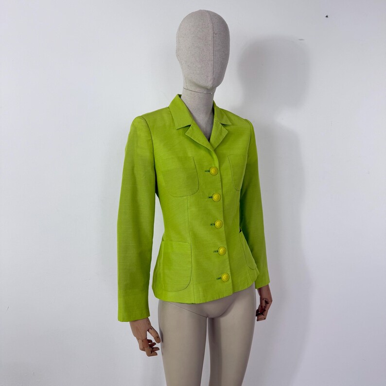 May include: A lime green blazer with a tailored fit, featuring a notched collar, two front pockets, and matching yellow buttons. The jacket is displayed on a mannequin, showcasing its structured design and vibrant color.