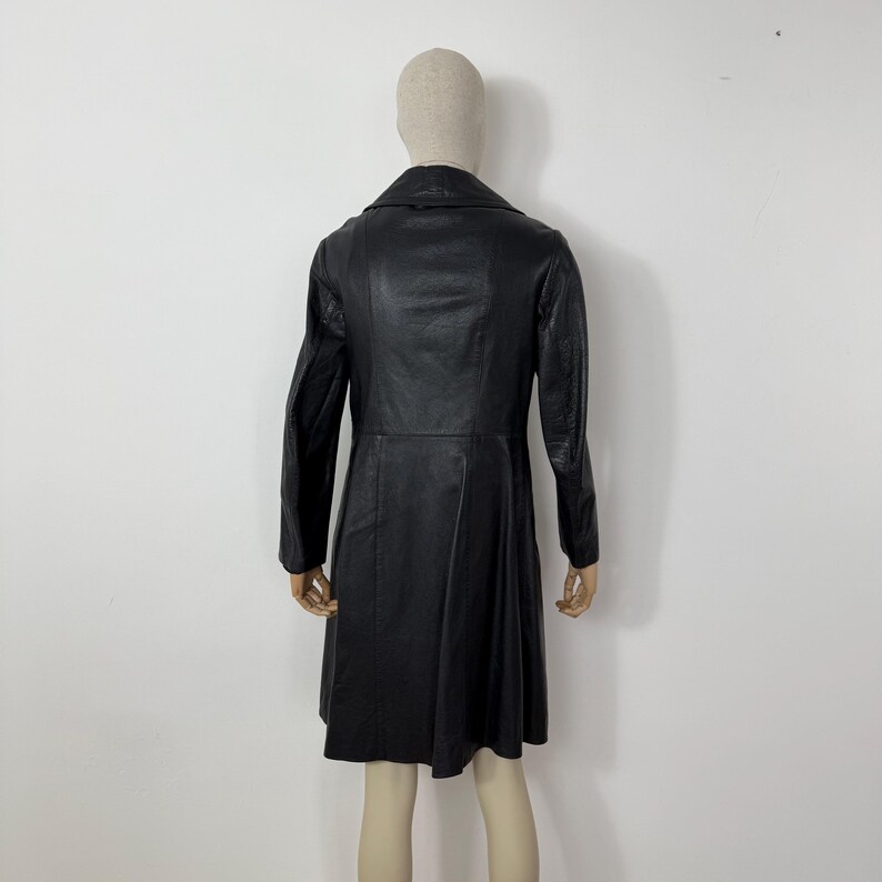 May include: A black leather coat with a classic design. The coat features a notched collar, long sleeves, and a flared skirt. The coat is displayed on a mannequin against a plain white background.