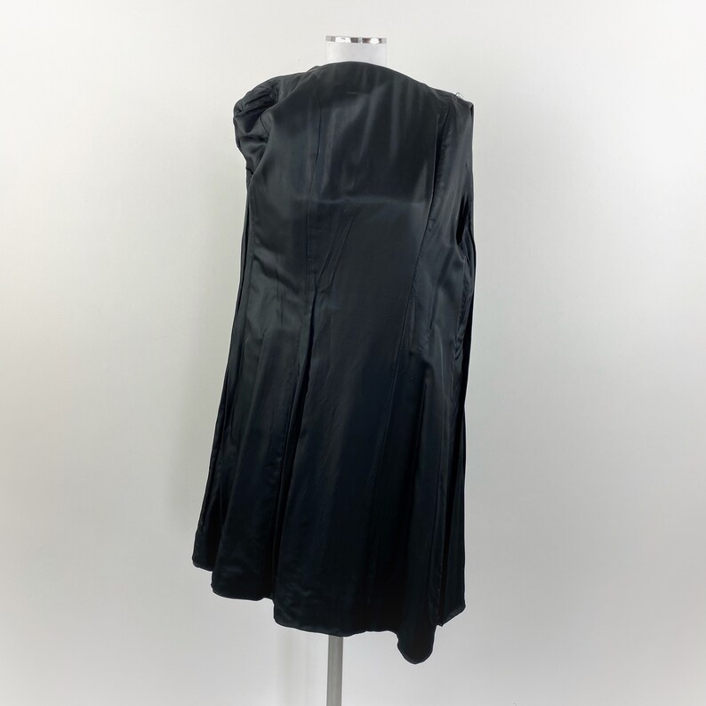 May include: A black, long coat with a satin lining, displayed on a mannequin. The coat is open, revealing the interior lining and construction. The coat's design features a classic, tailored silhouette.