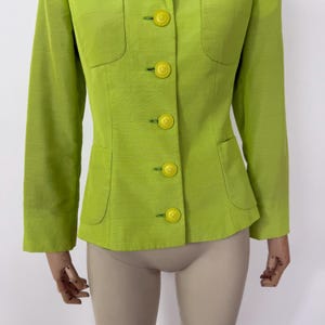 May include: A lime green blazer with a tailored fit. The jacket features a notched collar, two front pockets, and bright yellow buttons. The long sleeves and structured design create a classic silhouette. The fabric has a subtle texture.