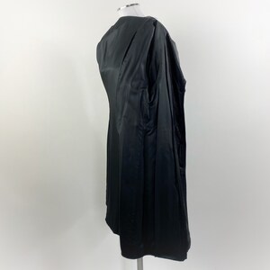 May include: A black coat with a satin-like sheen, displayed on a mannequin. The coat is long, with a tailored fit and a visible interior lining. The garment is designed with a classic silhouette.