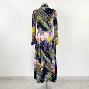 Puede incluir: Un vestido largo de manga larga con fondo negro y estampado floral colorido. El vestido tiene cuello alto y un corpi&ntilde;o ajustado. La falda es amplia y fluida.