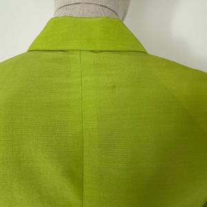 May include: A close-up of the back of a lime green blazer. The blazer has a notched collar and a subtle sheen. The fabric appears to be silk or a silk blend. The blazer is displayed on a mannequin.