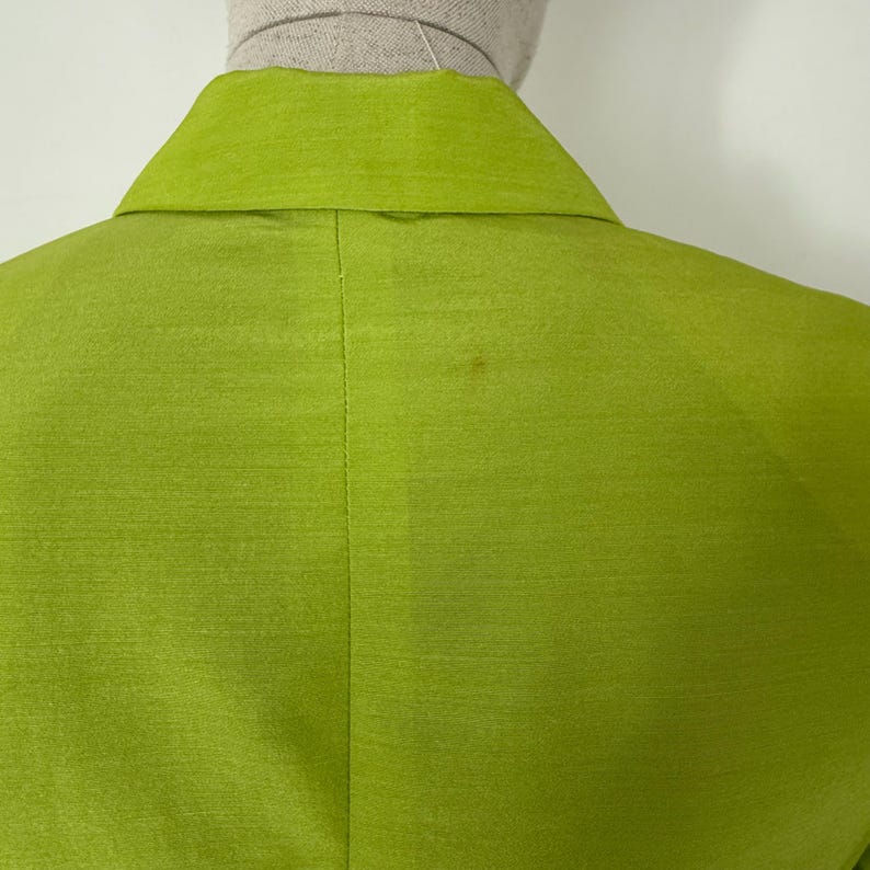 May include: A close-up of the back of a lime green blazer. The blazer has a notched collar and a subtle sheen. The fabric appears to be silk or a silk blend. The blazer is displayed on a mannequin.