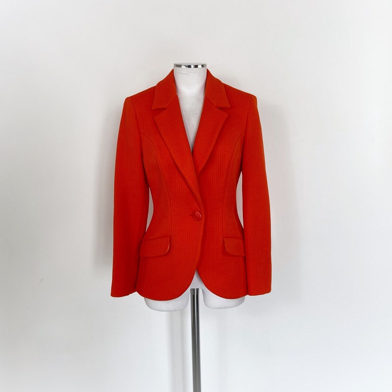 May include: A bright orange blazer with a single button closure and two pockets. The blazer is tailored and has a fitted silhouette.