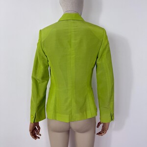 May include: A lime green blazer with a two-button closure and long sleeves. The blazer is displayed on a mannequin, showcasing the back of the garment. The fabric has a subtle sheen, suggesting a silk or similar material. The blazer has a classic tailored design.