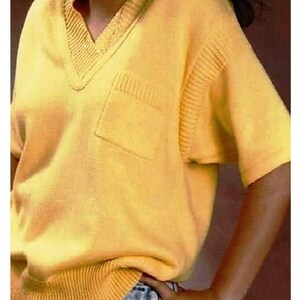 May include: A yellow short-sleeved knitted sweater with a v-neck and a patch pocket on the left side.