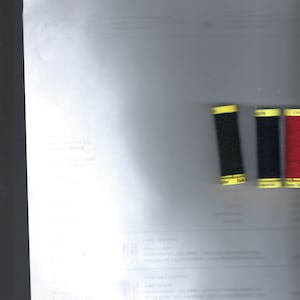 May include: Three spools of thread, one red, one black, and one black with a yellow label. The labels on the spools read "Polyester 150m", "Polyester 150m", and "Elasthan".