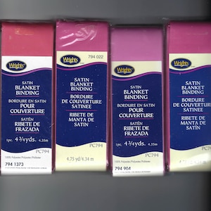 May include: Four spools of Wrights satin blanket binding in shades of pink and purple. Each spool has text in English, French, and Spanish. The spools are labeled with the product name, color, and length of 4.75 yards or 4.34 meters.
