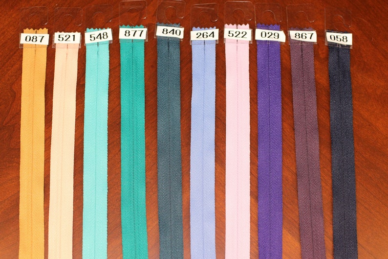 May include: A close-up of ten different colors of zipper tape, each labeled with a number. The colors are: yellow, peach, light blue, teal, dark blue, light blue, pink, purple, brown, and dark blue.