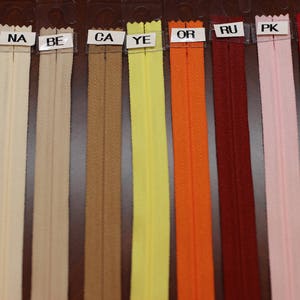 Puede incluir: Una selecci&oacute;n de cintas de cremallera en varios colores, incluyendo blanco, beige, marr&oacute;n, amarillo, naranja, rojo, rosa y rojo. Las cintas de cremallera est&aacute;n etiquetadas con letras, incluyendo WH, NA, BE, CA, YE, OR, RU, PK y RE.