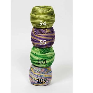 May include: Four balls of yarn stacked on top of each other. The top ball is green, the second ball is purple and green, the third ball is green, and the bottom ball is multi-colored. Each ball has a number printed on it: 94, 55, 101, and 109.