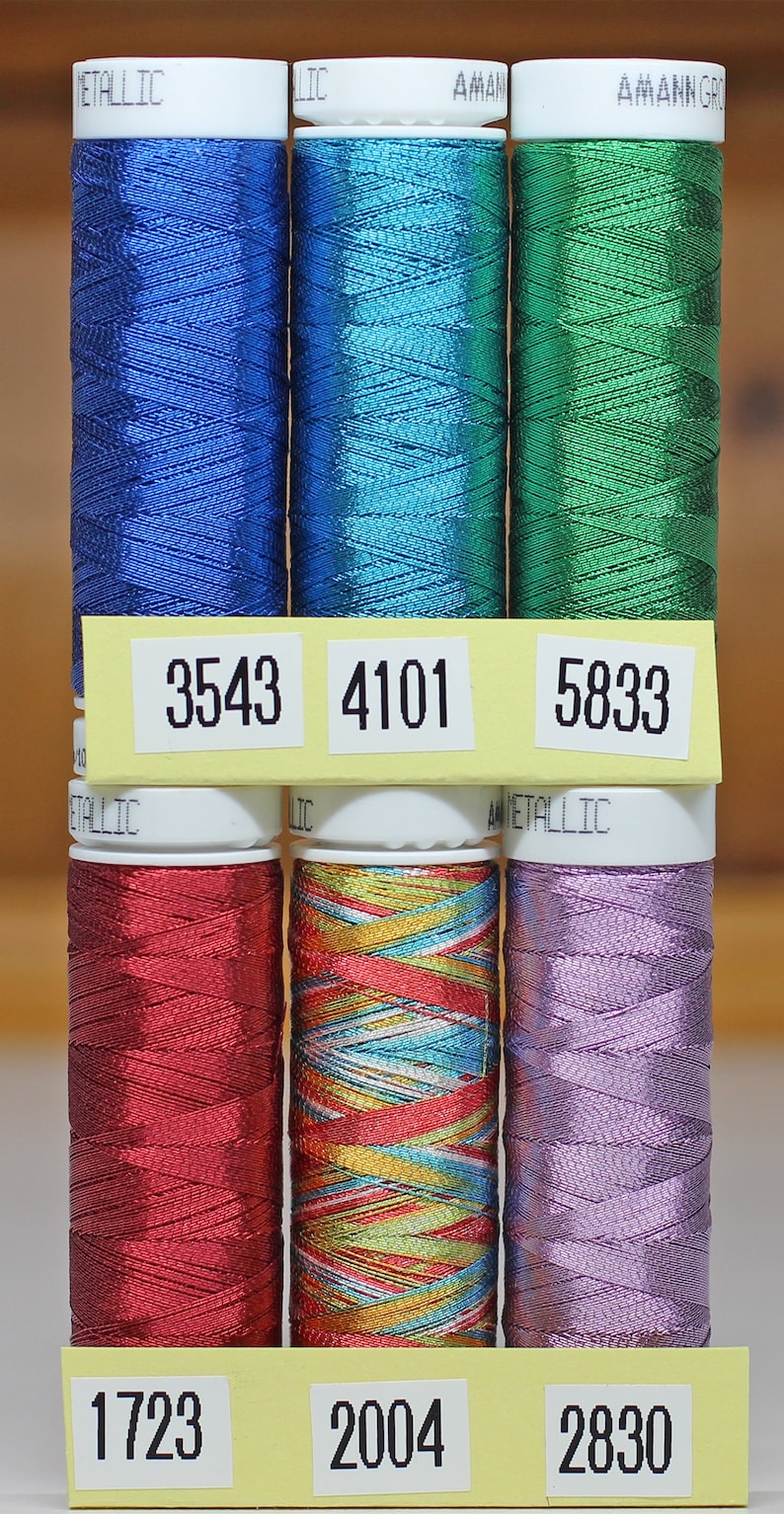 May include: Six spools of metallic thread in various colors, including blue, green, red, gold, and purple. Each spool has a white label with a number printed on it: 3543, 4101, 5833, 1723, 2004, and 2830.