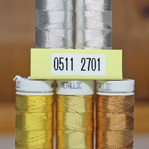 May include: Six spools of metallic thread, three silver and three gold. The spools are labeled with numbers: 0511, 2701, 0490, 2108, and 1134.