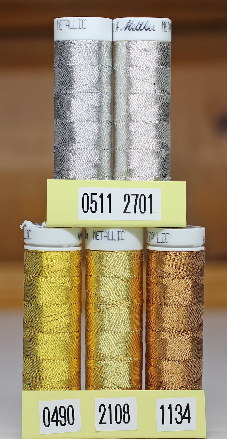May include: Six spools of metallic thread, three silver and three gold. The spools are labeled with numbers: 0511, 2701, 0490, 2108, and 1134.