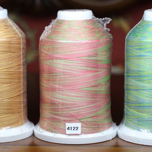 Könnte beinhalten: Drei Spulen mit Stickgarn, eine goldfarben, eine rosa und grün, und eine blau und grün. Die Spulen sind mit den Nummern 4044, 4122 und 4120 beschriftet.