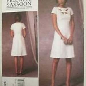 May include: A white dress sewing pattern with a scoop neckline and short sleeves. The pattern includes a decorative detail on the bodice. The pattern is for sizes 6-14.