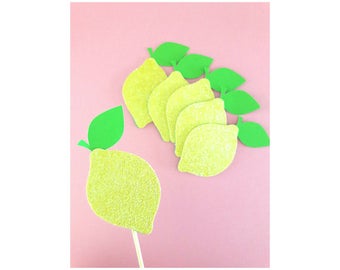 May include: A set of six yellow glitter lemon cupcake toppers with green leaves. The lemons are arranged in a semi-circle with the leaves facing outwards.