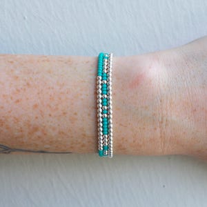 May include: A turquoise and silver beaded bracelet. The bracelet is made of small, round beads and is layered in a simple design.