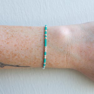 May include: A turquoise and silver beaded bracelet on a person's wrist.