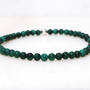 May include: A beaded bracelet featuring small, round, dark green malachite stones. The bracelet is strung on a flexible band and has a silver-colored clasp. The beads have a natural, marbled appearance.