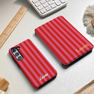 May include: Two phone cases with a red and pink striped pattern. The cases have the name "Lauren" written on them in gold lettering.