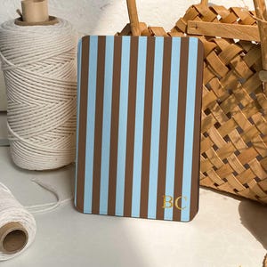 May include: A rectangular case with a blue and brown striped pattern. The initials "BC" are in gold on the lower right corner. A roll of white string and a woven basket are in the background.