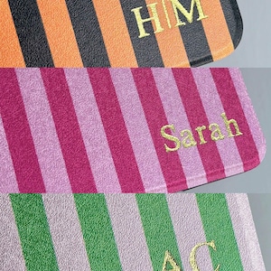 K&ouml;nnte beinhalten: Drei rechteckige Gegenst&auml;nde mit vertikalen Streifen und goldener Schrift. Der oberste Gegenstand ist orange und schwarz mit den Buchstaben HM. Der mittlere ist magenta und hellrosa mit dem Namen Sarah. Der untere ist gr&uuml;n und hellrosa mit den Buchstaben AC.