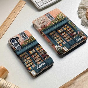 Op de afbeelding: Twee telefoonhoesjes met een boekwinkelontwerp. De hoesjes zijn beide roze en blauw met een boekenkast vol boeken. De tekst "BOOK SHOP" staat op de voorgevel van de winkel. De naam "Lauren" staat op elk hoesje.