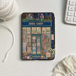 May include: A book shop storefront with a blue sign that reads "BOOK SHOP". The shop is decorated with flowers and has a green door. The storefront is covered in snow.
