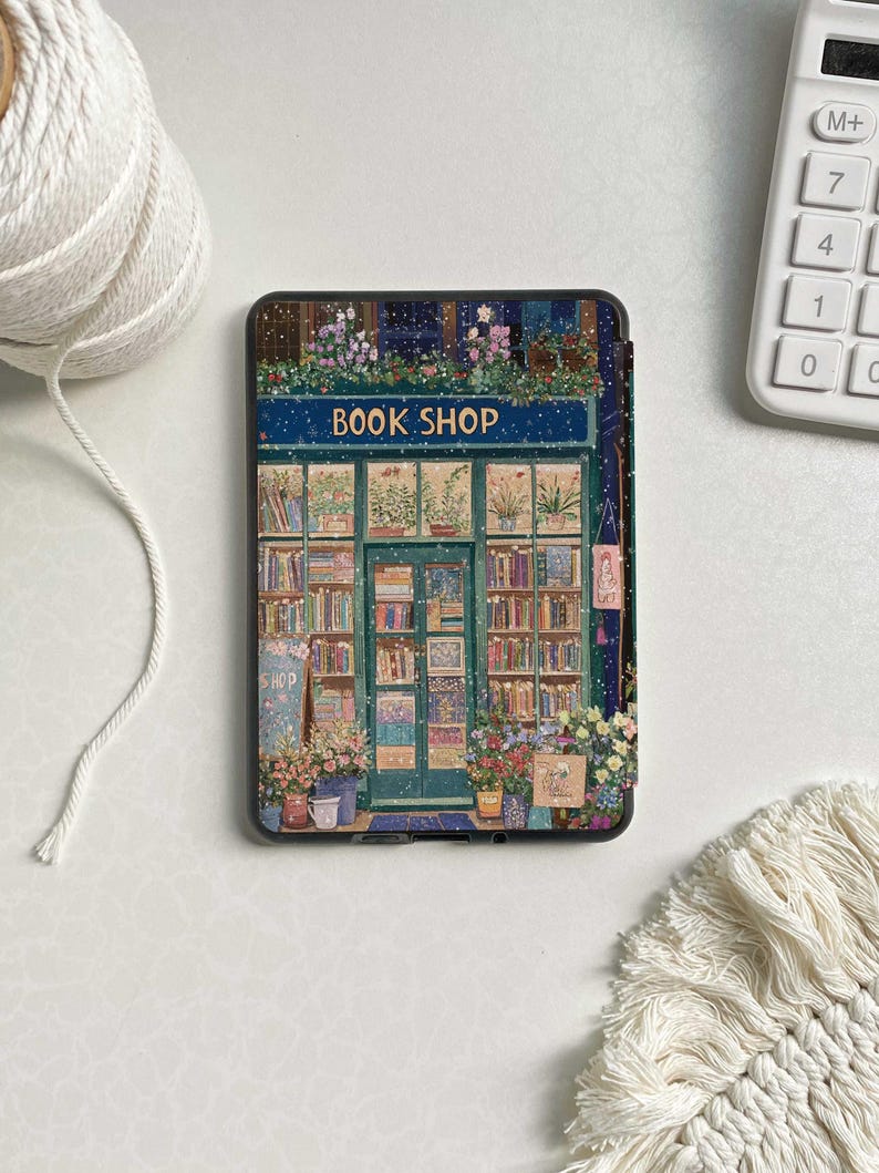 May include: A book shop storefront with a blue sign that reads "BOOK SHOP". The shop is decorated with flowers and has a green door. The storefront is covered in snow.